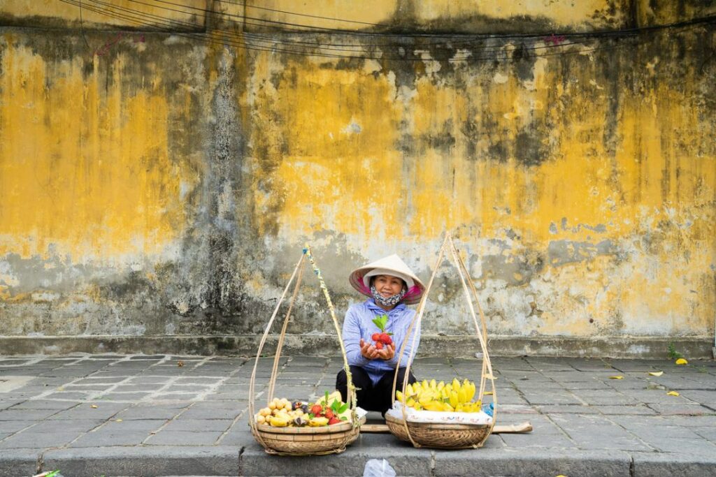 Venditrice di frutta con muro giallo alle spalle